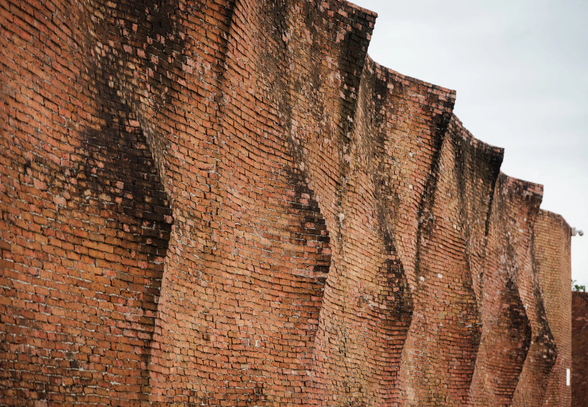 Undulating handmade brick boundary wall at Nongchok House